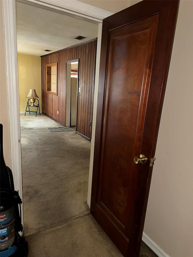 hallway with wooden walls, carpet flooring, baseboards, and visible vents