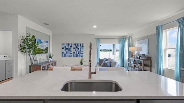 kitchen featuring visible vents, a kitchen island with sink, a sink, washer and dryer, and open floor plan