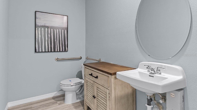 half bathroom featuring toilet, wood finished floors, baseboards, and a sink