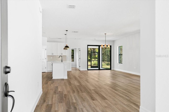 unfurnished living room with light wood-type flooring, visible vents, a notable chandelier, a sink, and baseboards