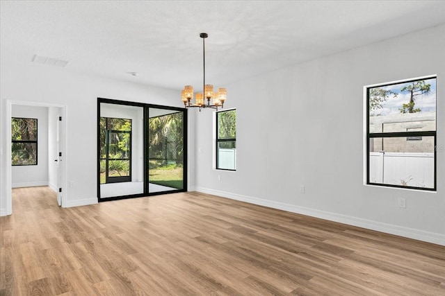 spare room featuring light wood finished floors, a notable chandelier, baseboards, and visible vents