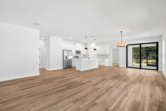 unfurnished living room with a chandelier, visible vents, light wood-type flooring, and a sink