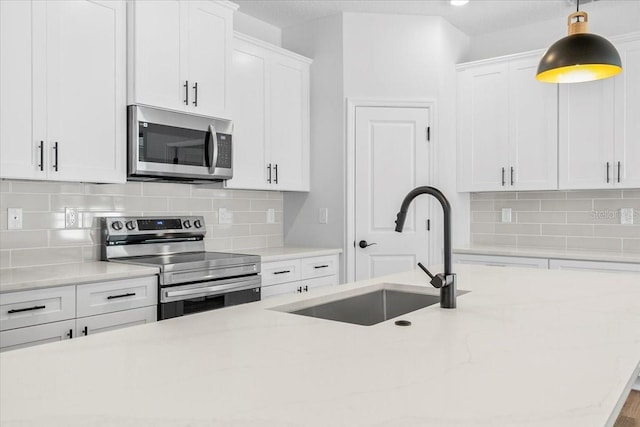 kitchen featuring a sink, decorative light fixtures, stainless steel appliances, white cabinets, and decorative backsplash