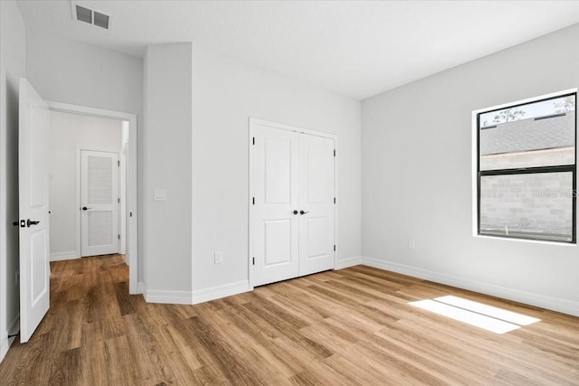 unfurnished bedroom with light wood-type flooring, baseboards, visible vents, and a closet