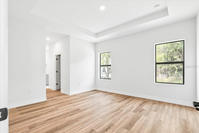 empty room featuring a raised ceiling, light wood-style flooring, recessed lighting, and baseboards