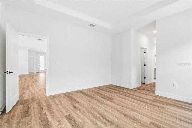 empty room with a tray ceiling, light wood-style flooring, baseboards, and visible vents