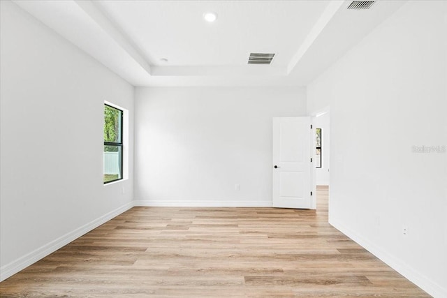 empty room with a tray ceiling, baseboards, visible vents, and light wood-type flooring