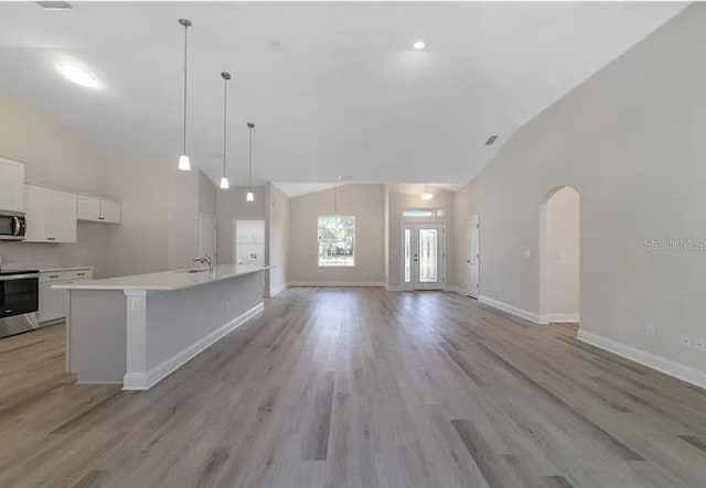 kitchen featuring stainless steel microwave, arched walkways, stove, white cabinets, and high vaulted ceiling