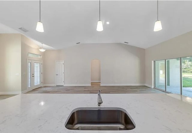 kitchen featuring visible vents, light stone countertops, open floor plan, lofted ceiling, and a sink