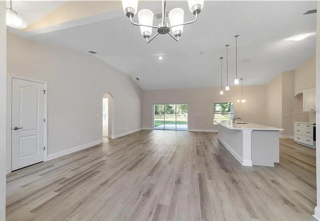 unfurnished living room with light wood finished floors, a notable chandelier, baseboards, and a sink