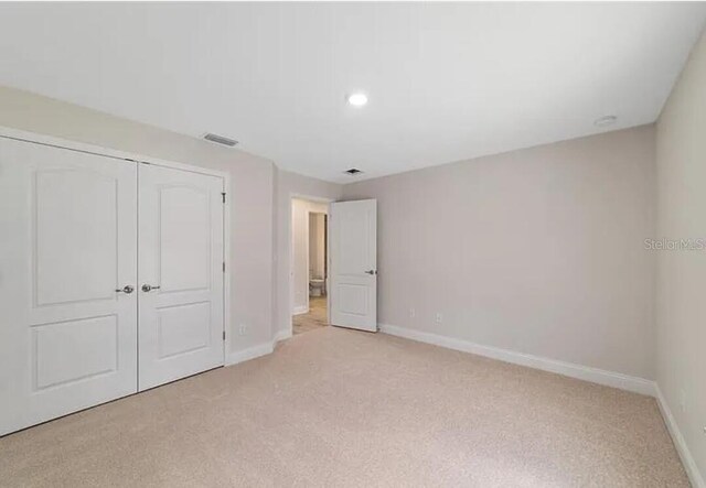 unfurnished bedroom featuring baseboards, visible vents, a closet, and light carpet