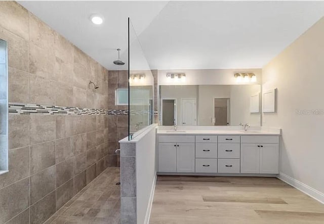 bathroom with double vanity, a walk in shower, wood finished floors, and a sink