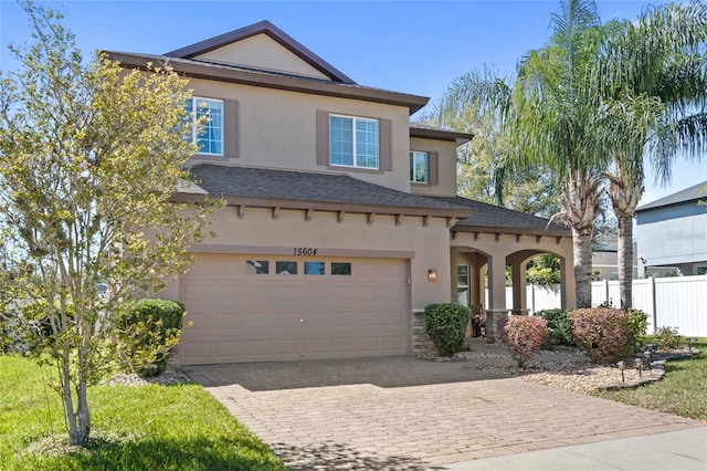 view of front of property with fence, an attached garage, stucco siding, stone siding, and decorative driveway