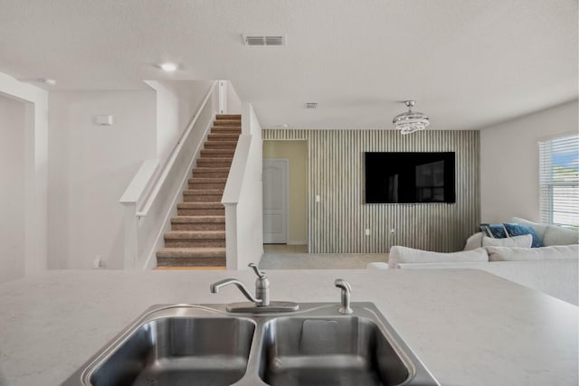 kitchen featuring visible vents, a sink, a textured ceiling, an accent wall, and open floor plan