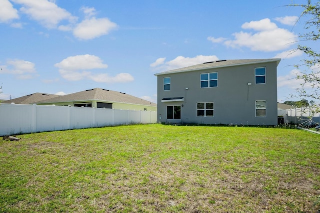 rear view of house with a lawn, a fenced backyard, and stucco siding