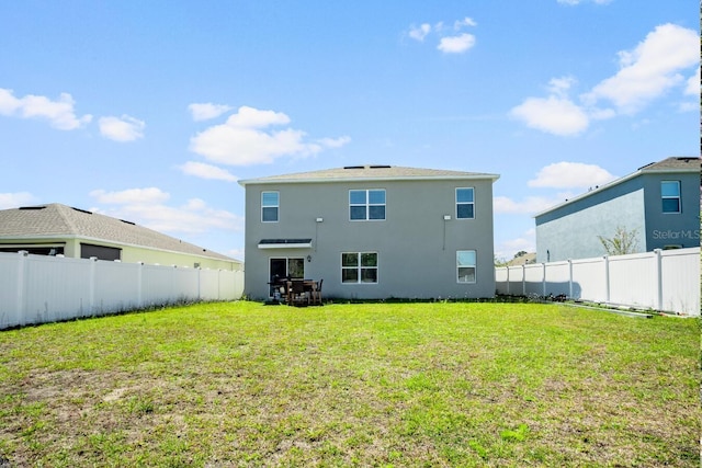 rear view of house with a fenced backyard, stucco siding, and a yard