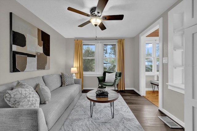 living area with visible vents, baseboards, dark wood-type flooring, and a ceiling fan