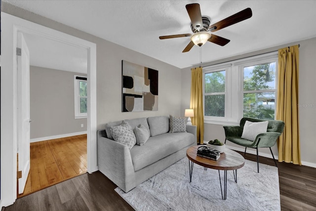 living room with baseboards, dark wood-type flooring, and ceiling fan