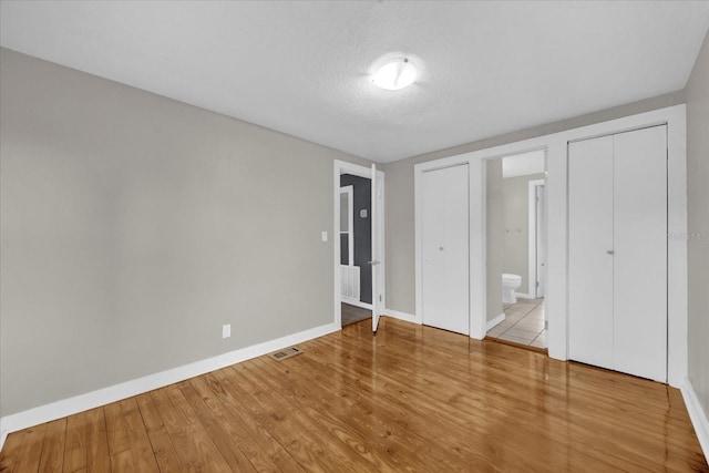 unfurnished bedroom featuring visible vents, baseboards, wood finished floors, ensuite bath, and a textured ceiling