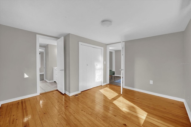 unfurnished bedroom with light wood-style floors, visible vents, a closet, and baseboards