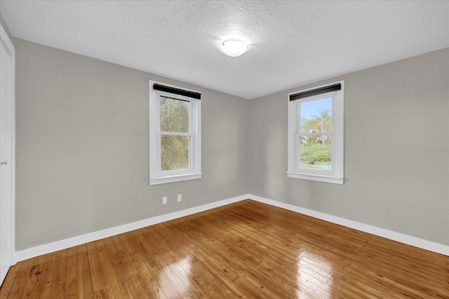 unfurnished room featuring hardwood / wood-style floors, baseboards, and a textured ceiling