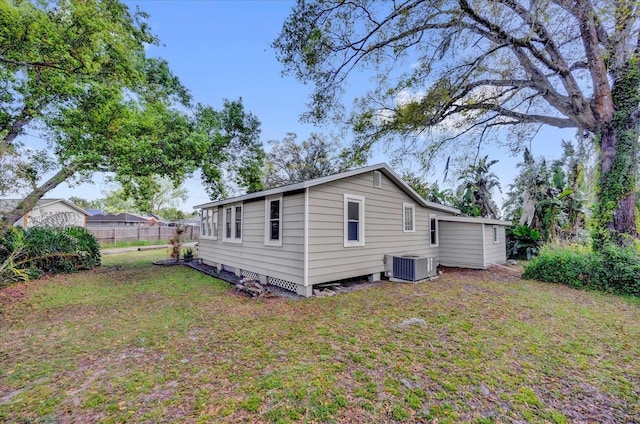 back of house with central air condition unit, a lawn, and fence