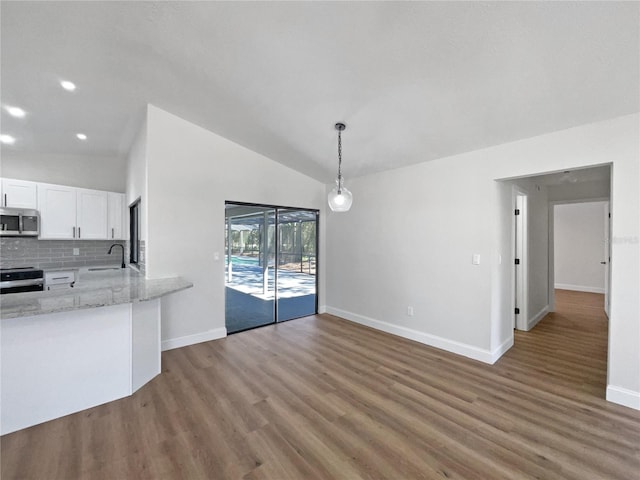 unfurnished dining area featuring a sink, wood finished floors, recessed lighting, baseboards, and vaulted ceiling