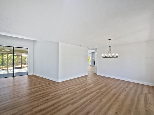 spare room with baseboards, wood finished floors, and a chandelier