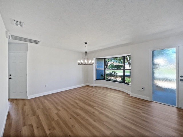 unfurnished dining area featuring a textured ceiling, wood finished floors, visible vents, and a chandelier