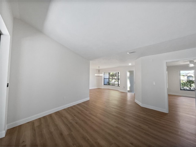 unfurnished living room with a notable chandelier, wood finished floors, visible vents, and baseboards