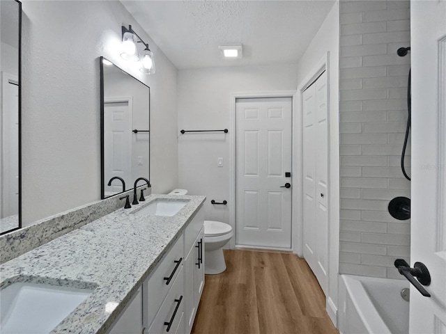 full bathroom with double vanity, toilet, wood finished floors, and a sink