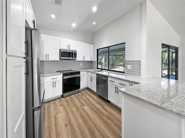 kitchen featuring a sink, stainless steel appliances, a peninsula, decorative backsplash, and light stone countertops