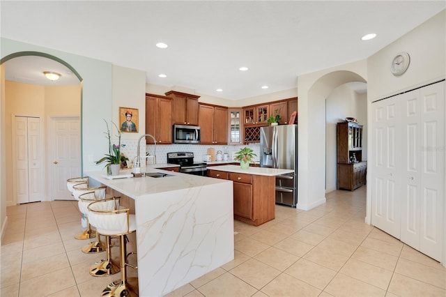 kitchen featuring light tile patterned floors, brown cabinetry, arched walkways, stainless steel appliances, and a center island