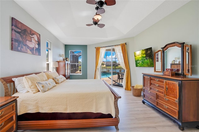 bedroom with a tray ceiling, access to outside, and light wood-type flooring