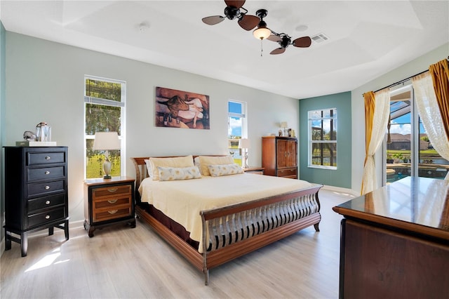 bedroom featuring a raised ceiling, light wood-style flooring, multiple windows, and visible vents