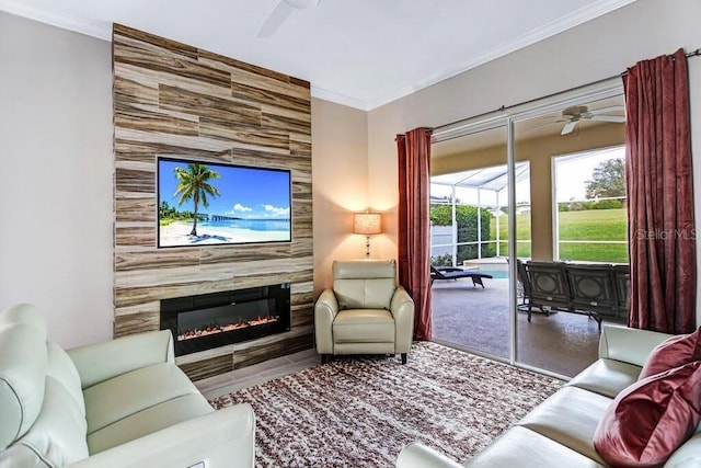 living room with an accent wall, crown molding, a large fireplace, and ceiling fan