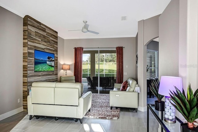 tiled living room featuring baseboards, visible vents, arched walkways, ceiling fan, and crown molding