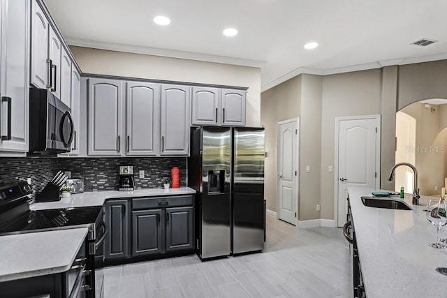 kitchen featuring crown molding, decorative backsplash, arched walkways, black appliances, and a sink