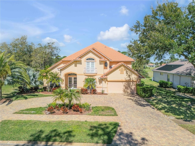 mediterranean / spanish-style home with a front lawn, a tile roof, stucco siding, french doors, and decorative driveway