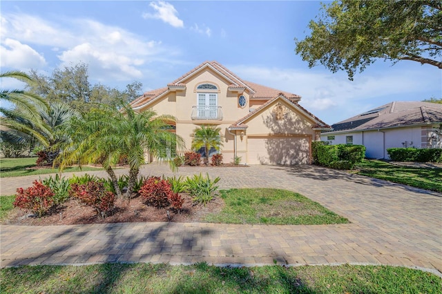 mediterranean / spanish-style home with stucco siding, a tiled roof, decorative driveway, and a garage