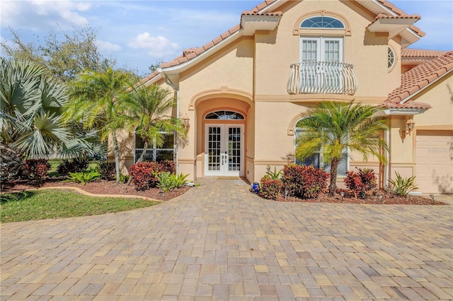 entrance to property featuring french doors, a balcony, stucco siding, and a tile roof