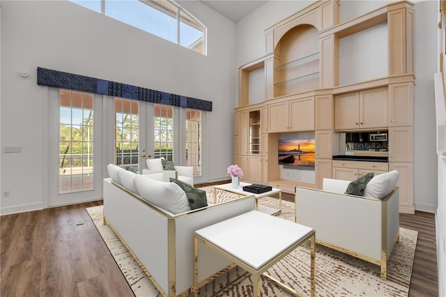 living room featuring french doors, baseboards, light wood-style floors, and a high ceiling