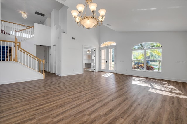 unfurnished living room featuring wood finished floors, baseboards, an inviting chandelier, stairs, and french doors