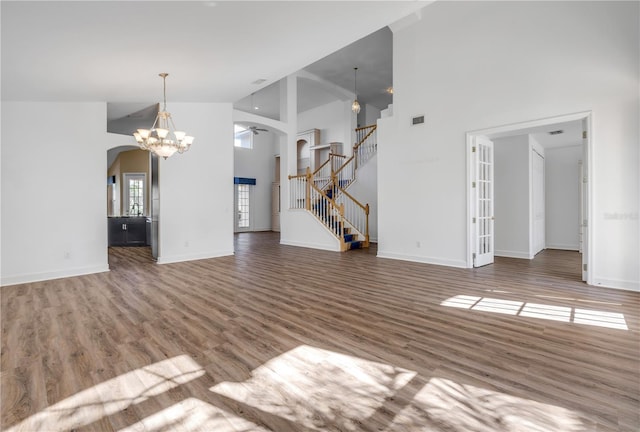 unfurnished living room with high vaulted ceiling, wood finished floors, arched walkways, an inviting chandelier, and stairs