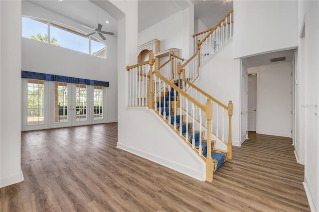 stairway with wood finished floors, a ceiling fan, baseboards, visible vents, and a high ceiling