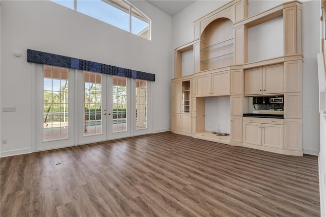 unfurnished living room with baseboards, a towering ceiling, and wood finished floors