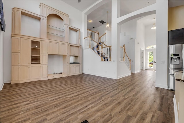 unfurnished living room featuring baseboards, stairway, a towering ceiling, wood finished floors, and arched walkways