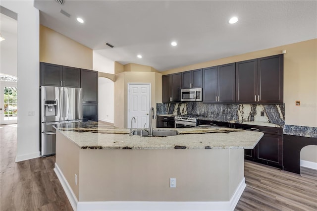 kitchen featuring a sink, light stone counters, appliances with stainless steel finishes, decorative backsplash, and vaulted ceiling