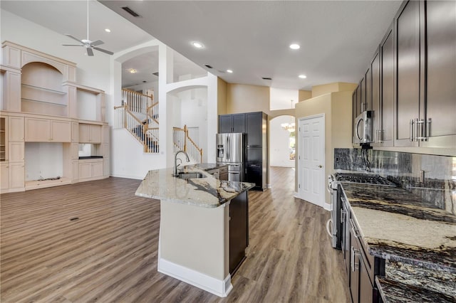 kitchen featuring a sink, stainless steel appliances, arched walkways, and light stone countertops