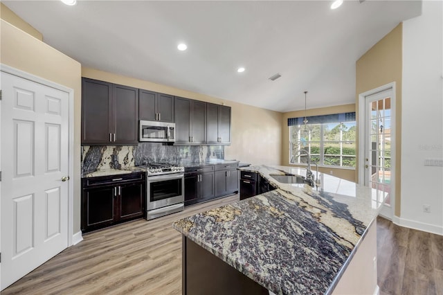 kitchen featuring light stone countertops, lofted ceiling, a sink, appliances with stainless steel finishes, and backsplash